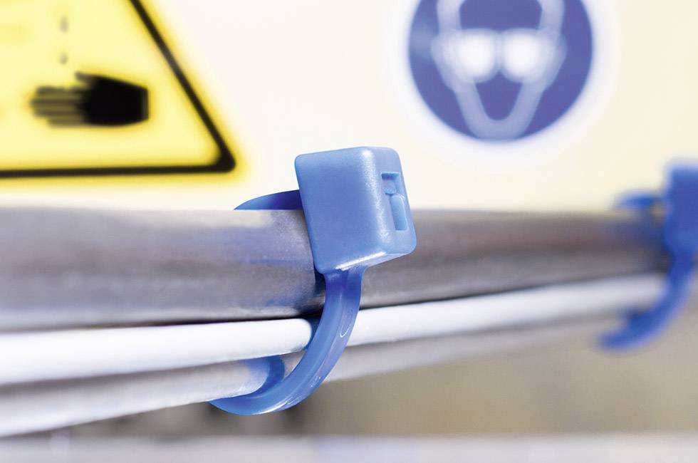Nahaufnahme eines blauen Kabelbinders, der mehrere Kabel an einer Stange befestigt. Im Hintergrund ein verschwommenes Warnschild.