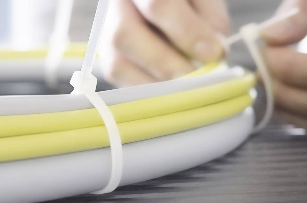 Nahaufnahme von zwei Händen, die gelbe und weiße Kabel mit einem weißen Kabelbinder zusammenbinden.