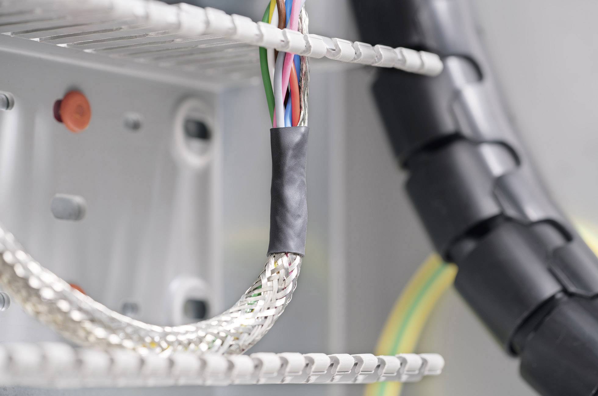 Ein Bündel elektrischer Kabel ist geordnet in einem Schaltschrank verlegt. Einige Kabel sind mit schwarzem Gummi umhüllt.