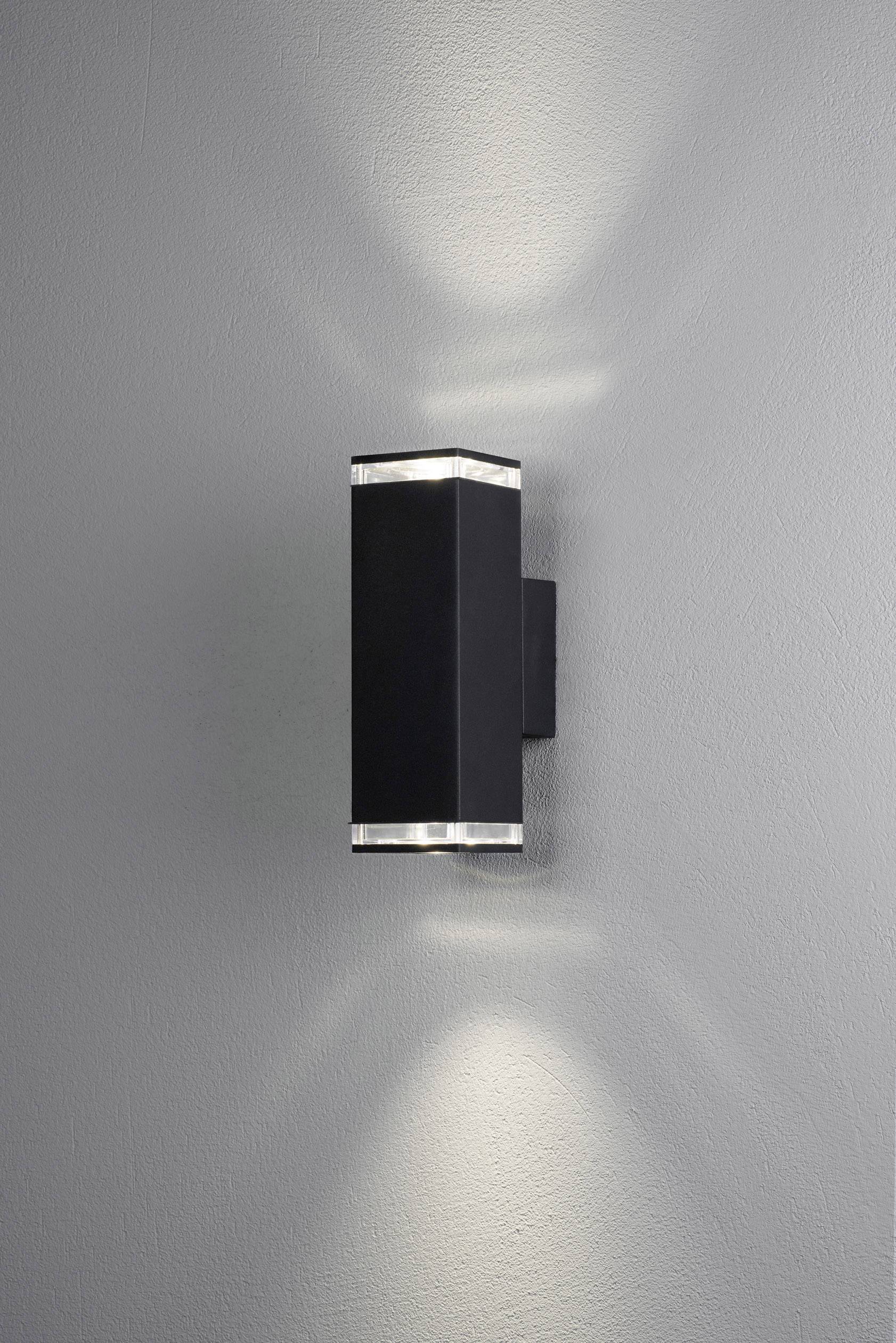 Schwarze, rechteckige Wandleuchte an grauer Wand, strahlt Licht nach oben und unten, erzeugt weiche Lichtkegel.
