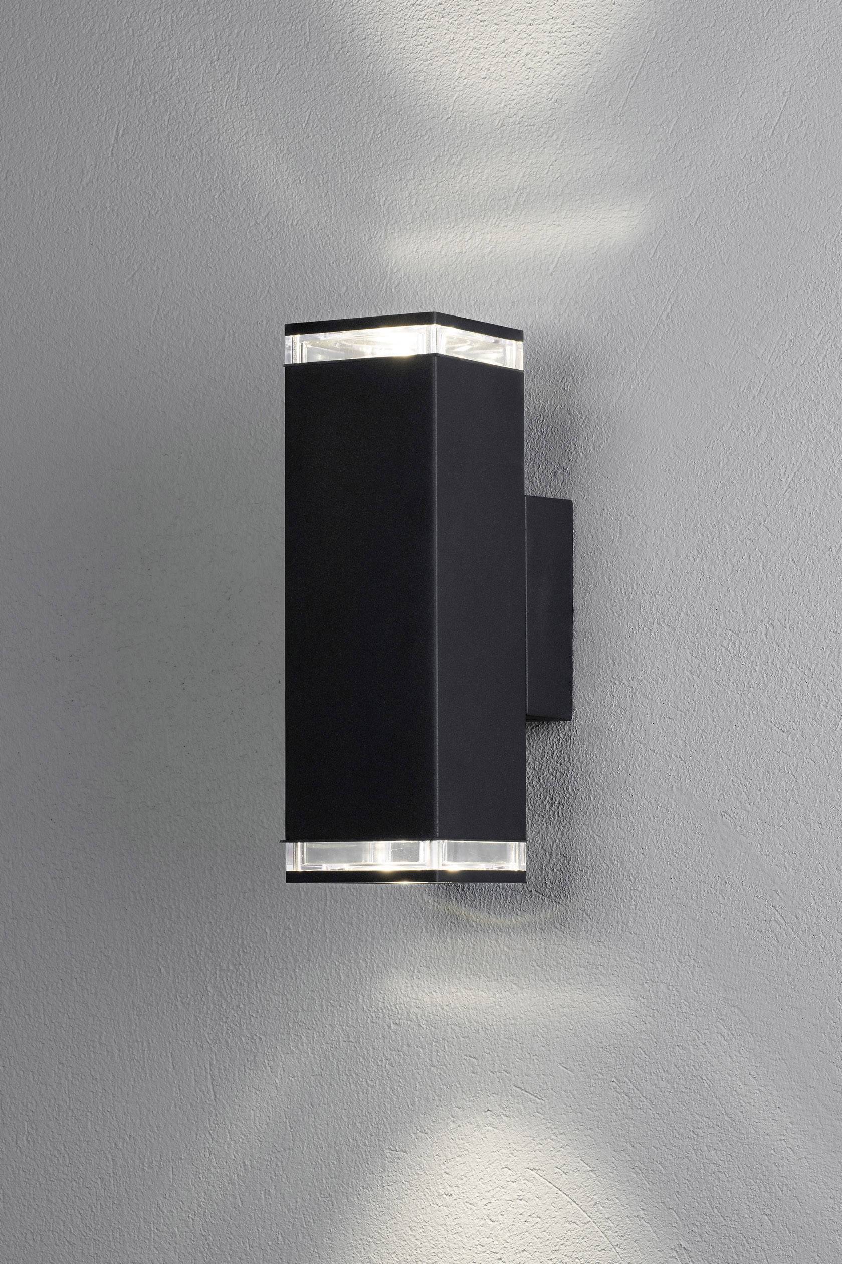 Schwarze, wandmontierte Leuchte mit oben und unten austretendem Licht, erzeugt ein elegantes Muster auf grauer Wand.