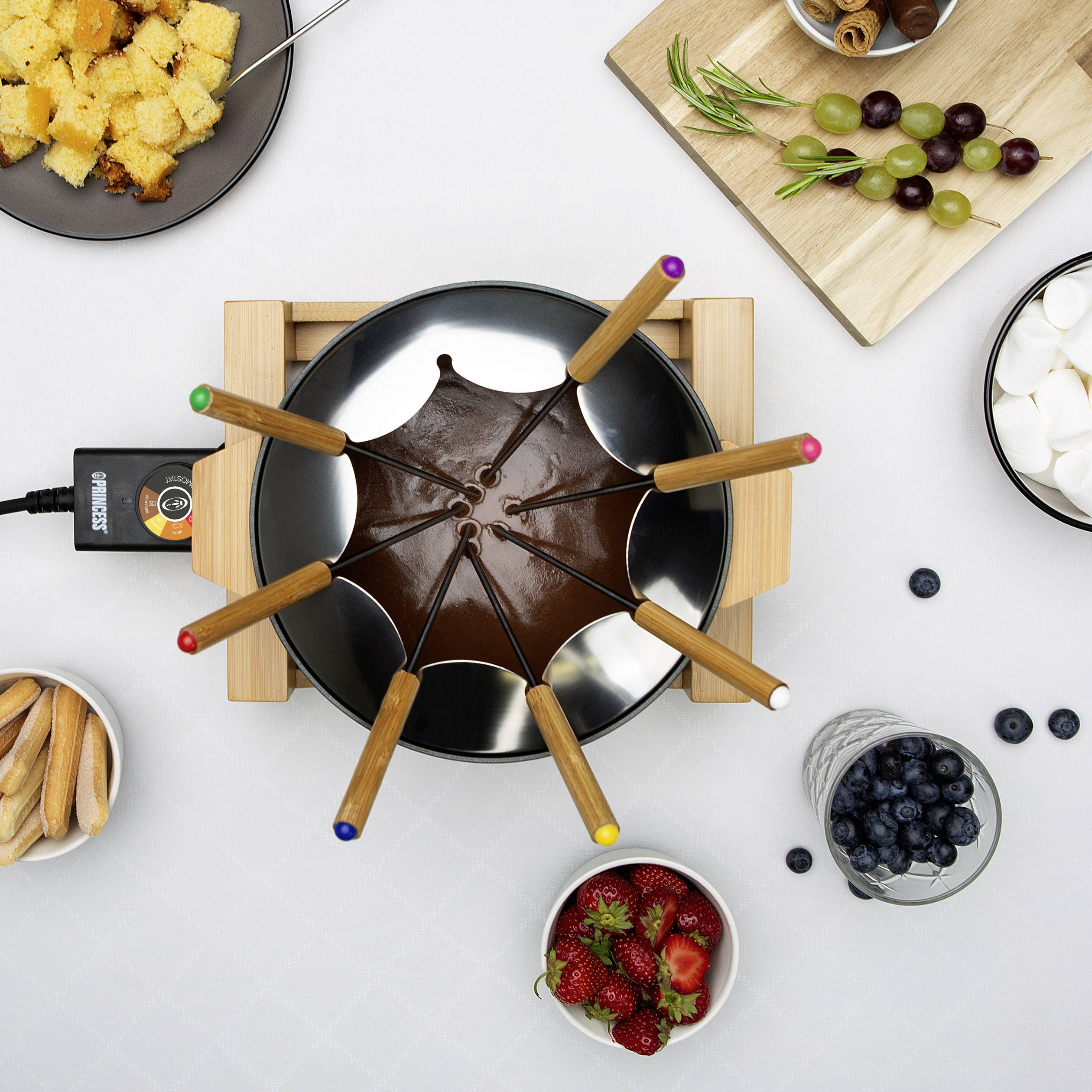 Ein Schokoladenfondue ist umgeben von Früchten, Keksen, Brot und Marshmallows auf einem Tisch, bereit zum Eintauchen.