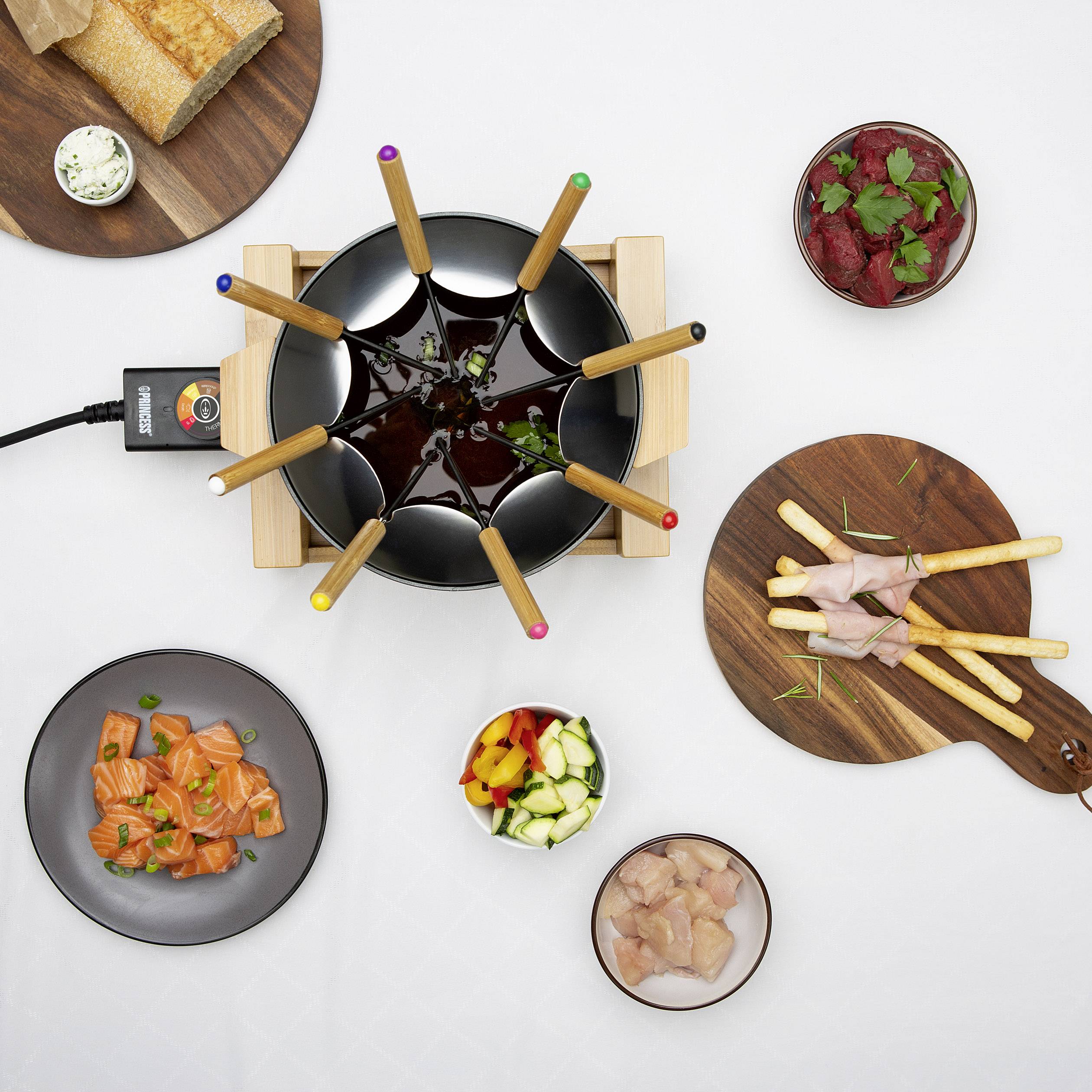 Fondue mit Gemüse, Fleisch, Brot und Soßen auf einem Tisch. Sechs Gabeln stecken im Fonduetopf.