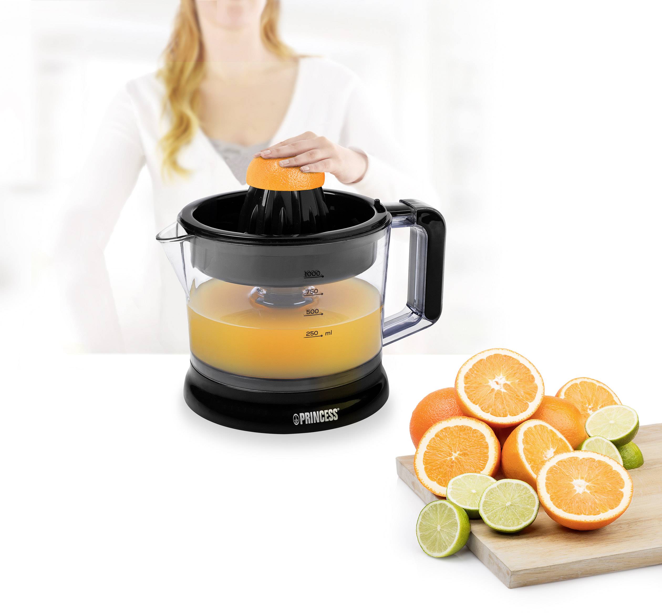 Eine Frau presst eine Orange mit einem elektrischen Entsafter. Daneben liegt ein Brett mit geschnittenen Orangen und Limetten.