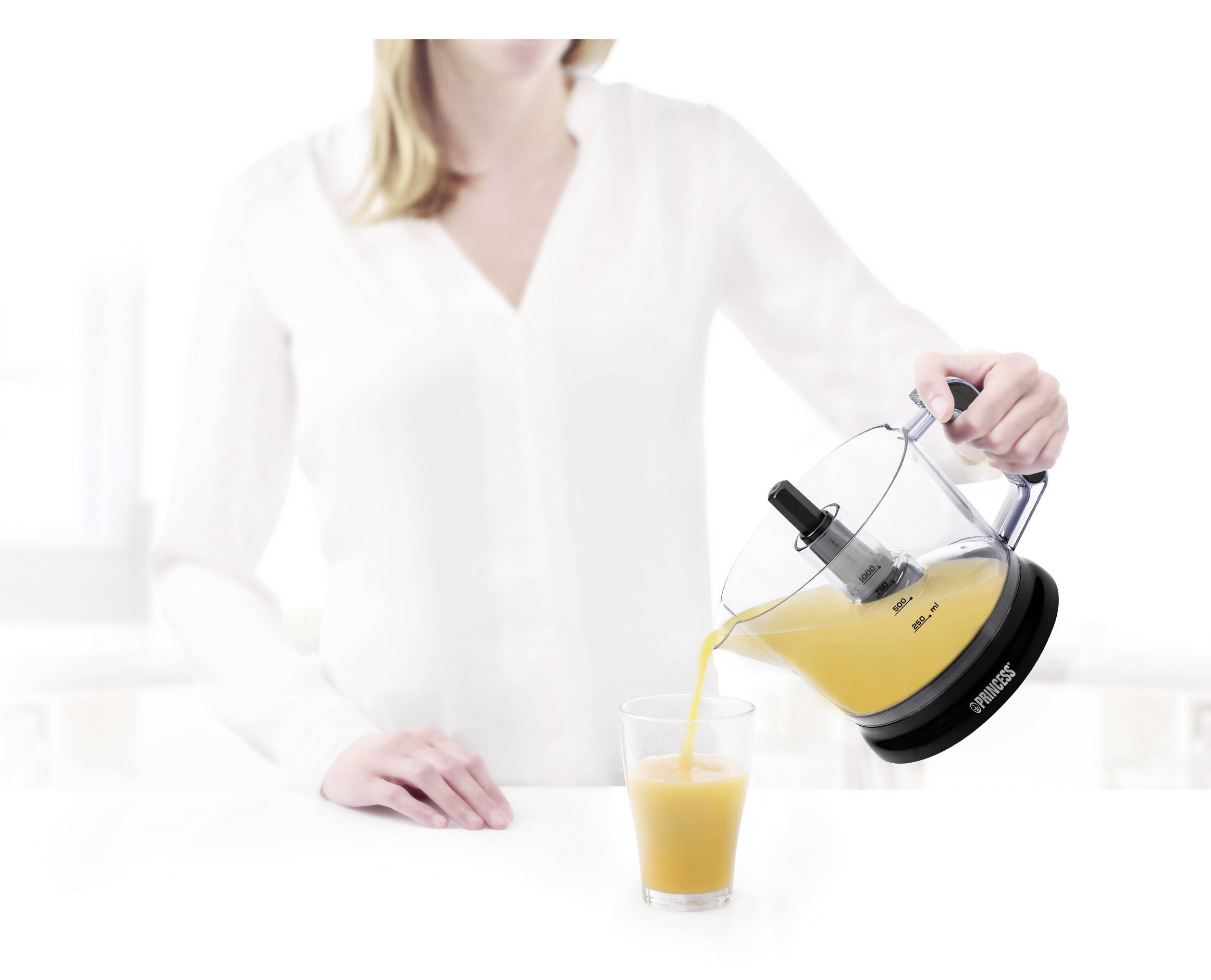 Frau gießt frisch gepressten Orangensaft aus einem Entsafter in ein Glas. Der Entsafter ist elektrisch und auf einer hellen Küche platziert.