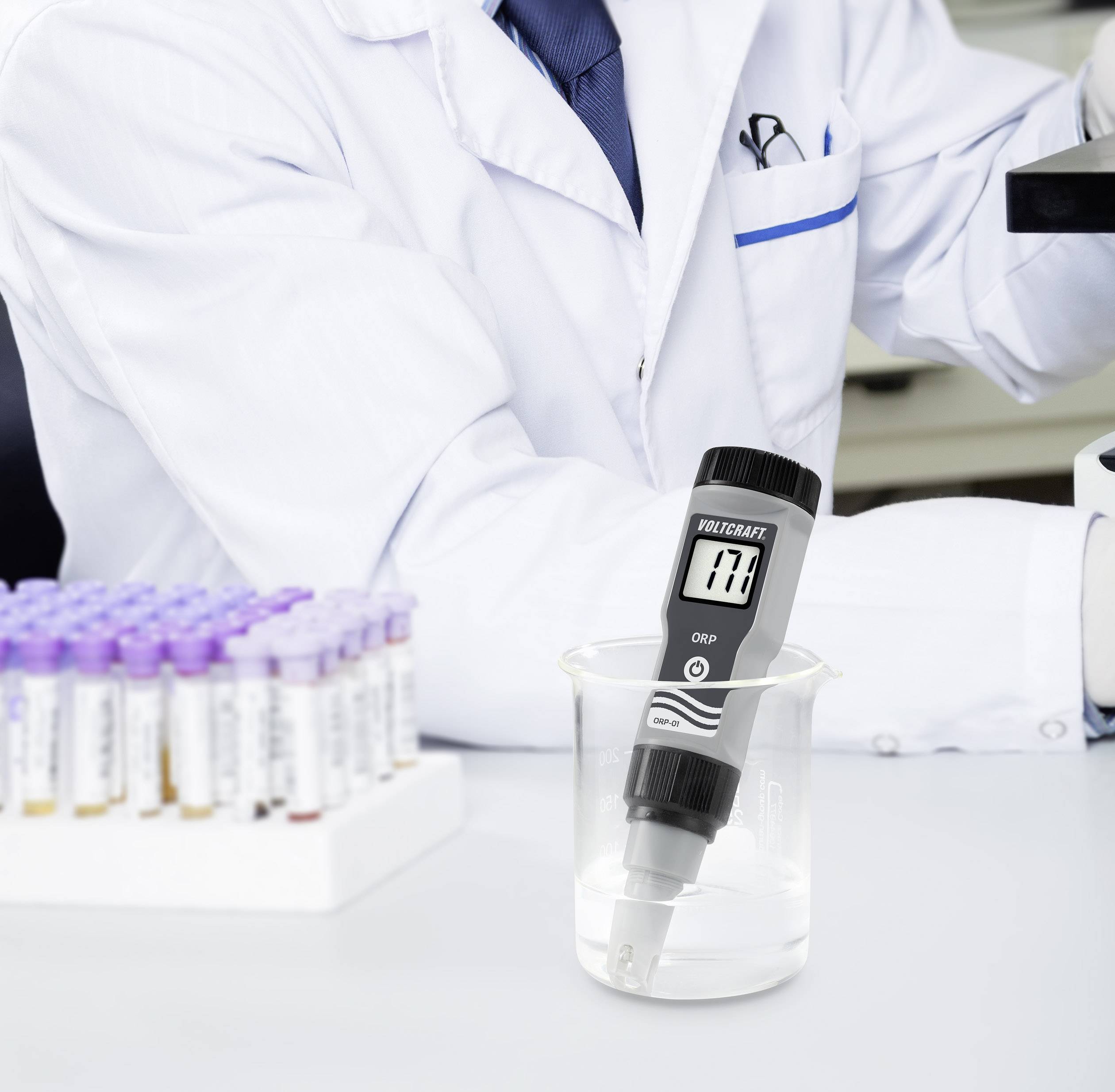 Ein Wissenschaftler in einem weißen Kittel misst den pH-Wert von Flüssigkeit in einem Becherglas mit einem digitalen pH-Meter.