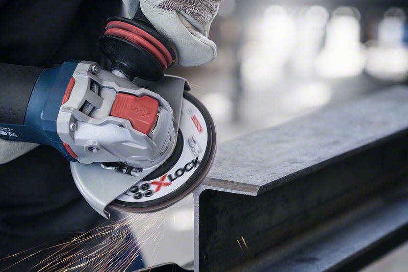 Eine Hand hält einen Winkelschleifer mit Funkenflug, während er an einem Metallstück arbeitet. Schutzhandschuhe sind sichtbar.