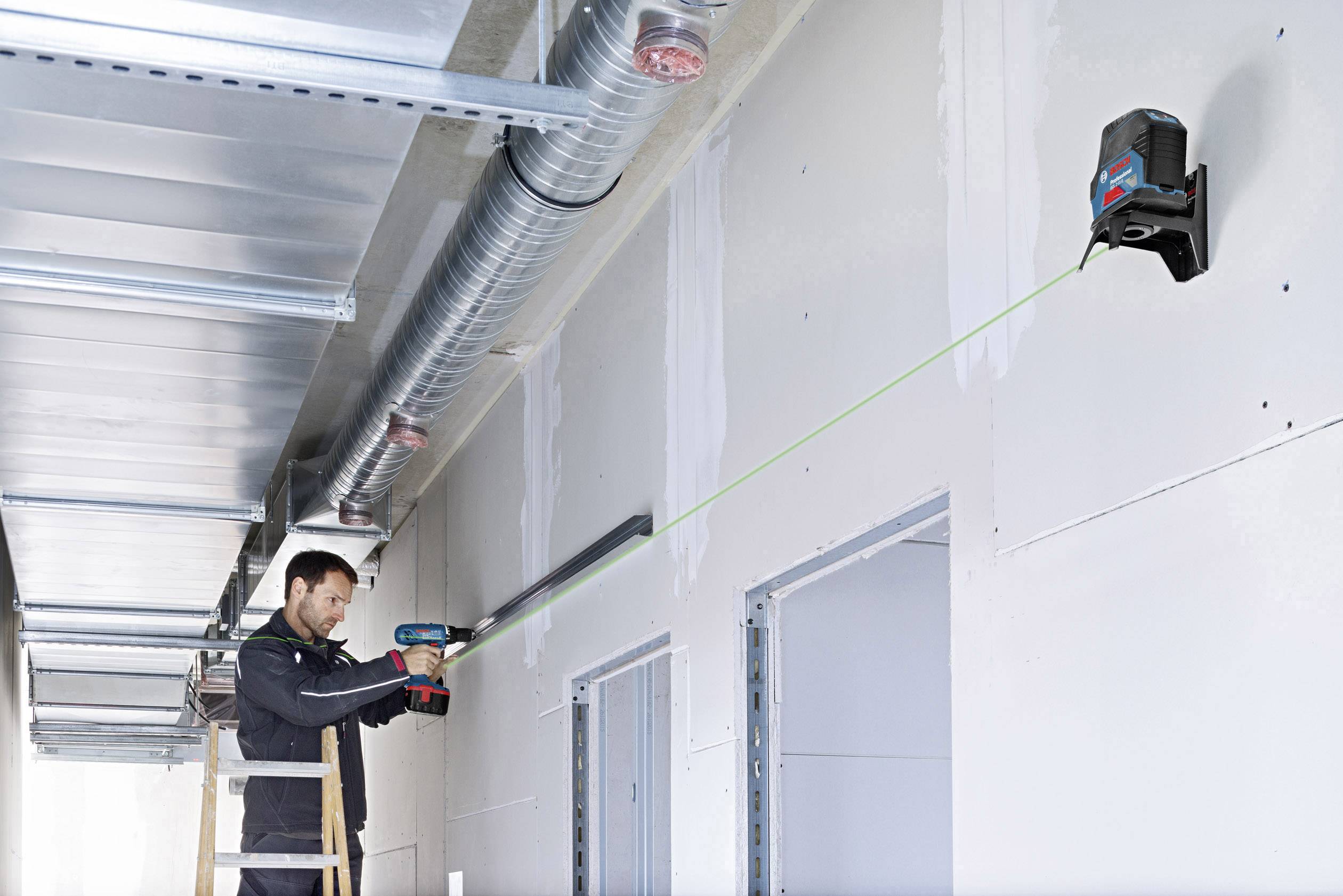 Eine Person arbeitet an einer Wandinstallation mit einem Werkzeug, das eine grüne Laserlinie projiziert, um eine präzise Ausrichtung sicherzustellen.