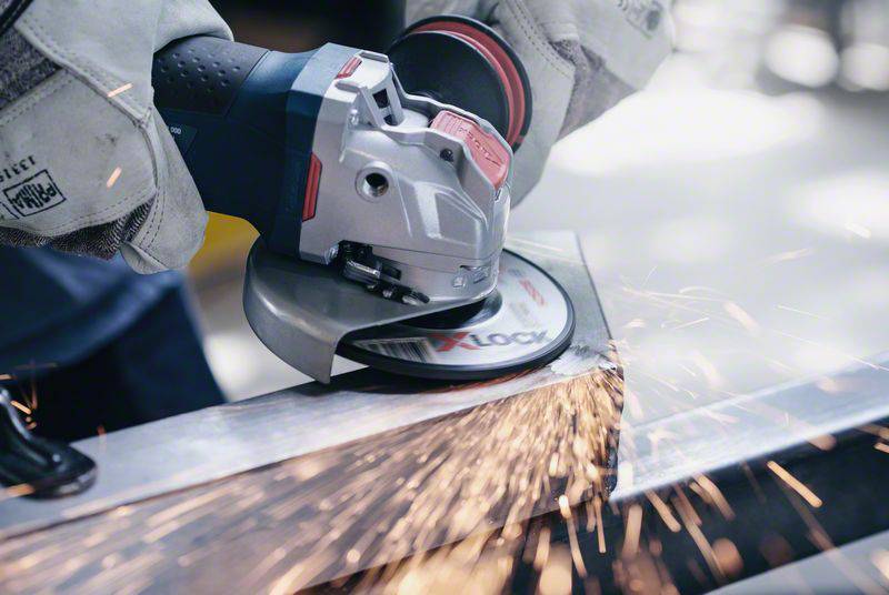 Eine Person schleift mit einem Winkelschleifer Metall. Funken fliegen vom Schleifpunkt, was intensives Arbeiten zeigt.