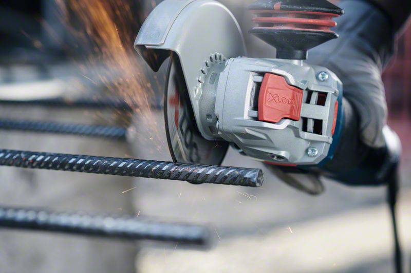 Eine Person schneidet Metallstäbe mit einem Winkelschleifer. Funken fliegen vom Schnittpunkt. Schutzkleidung wird getragen.