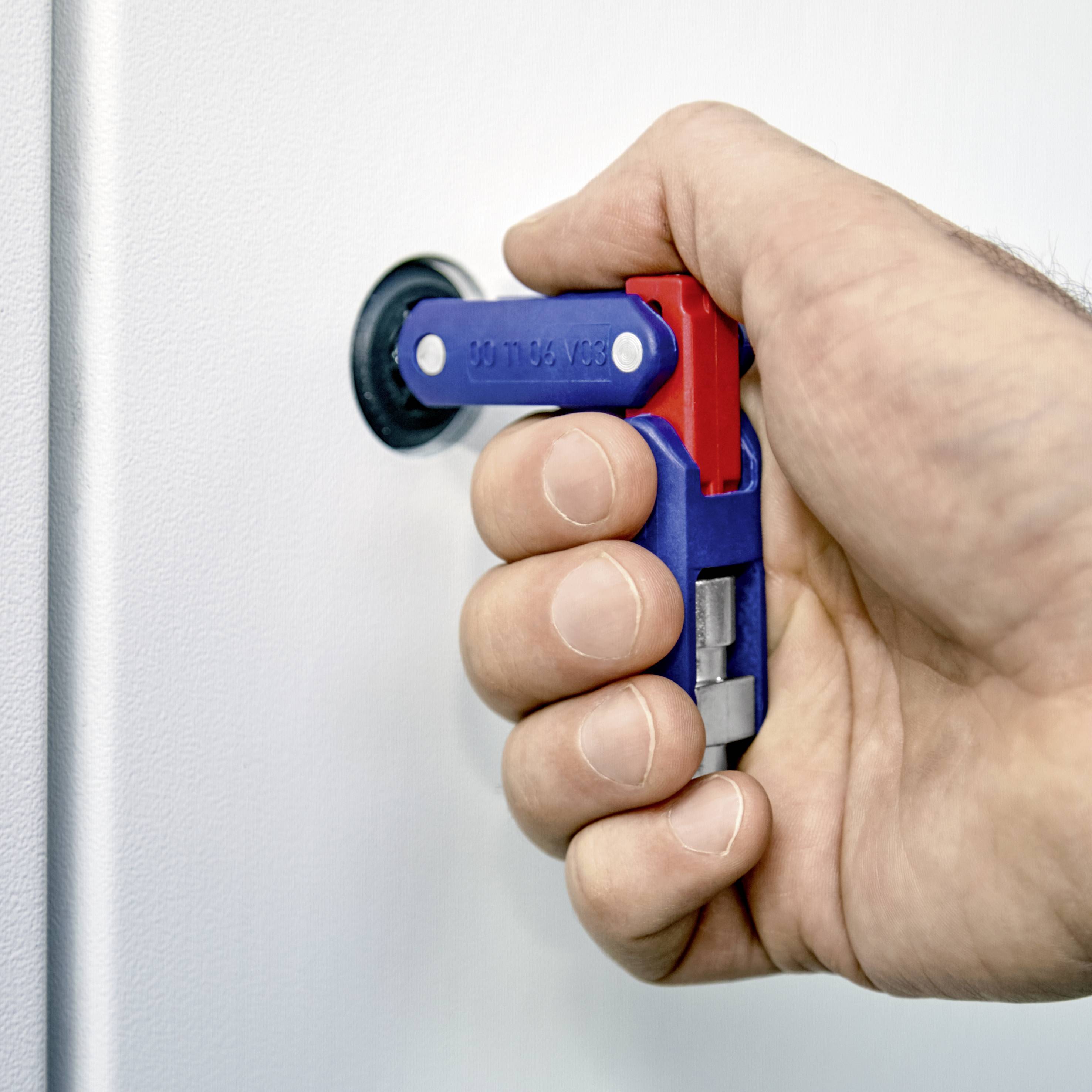 Hand dreht blauen und roten Griff, um einen zylindrischen Riegel in eine Schließposition zu bewegen. Wand und Hintergrund unscharf.
