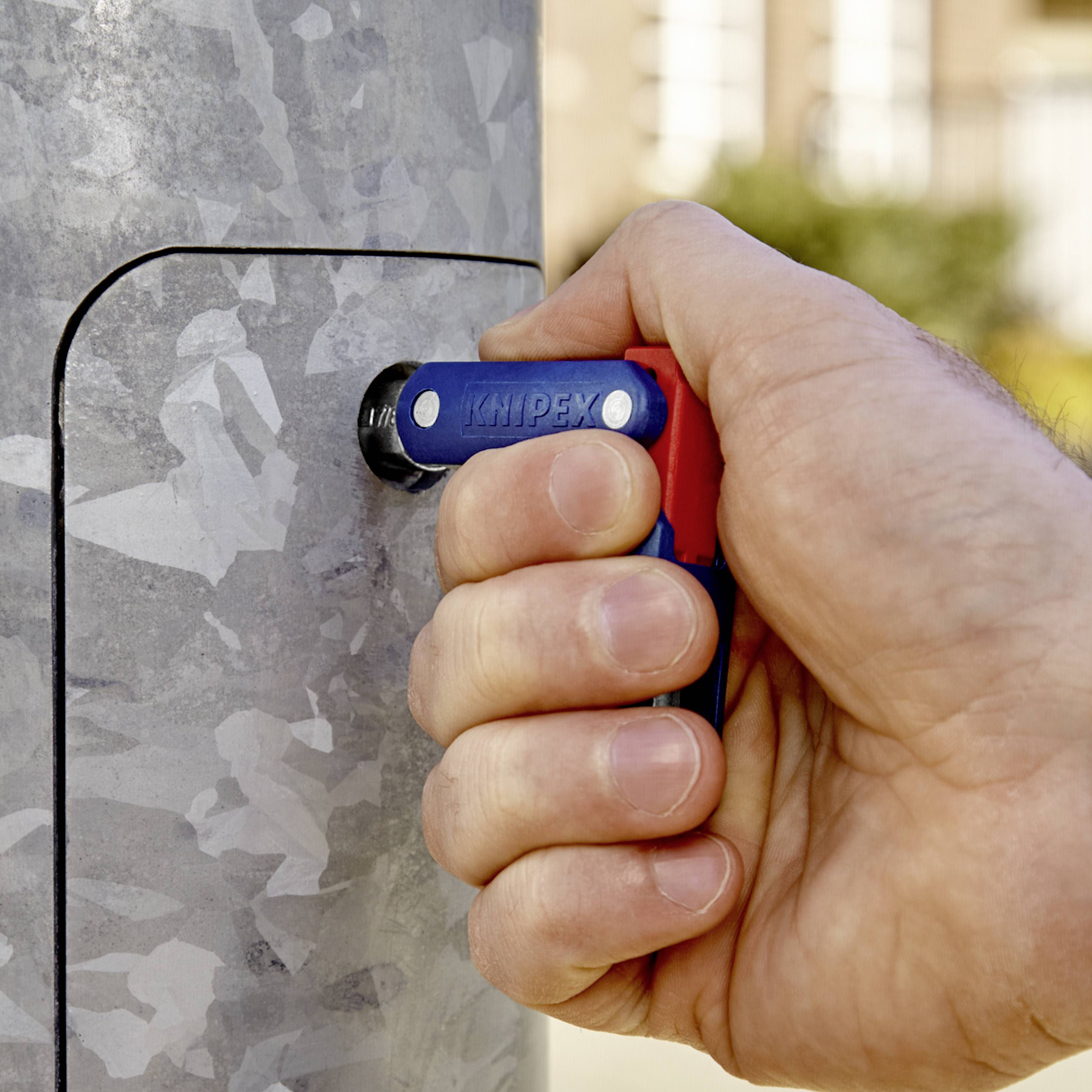 Eine Hand hält einen mit 'Knipex' beschrifteten Rohrsteckschlüssel und dreht damit das Schloss eines metallenen Stromkasten-Deckels.