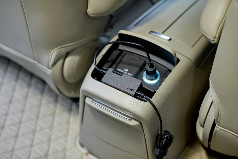 Ein schwarzes Kabel ist an eine Steckdose im Rücksitzbereich eines Autos angeschlossen, oberhalb einer geschlossenen Ablage.