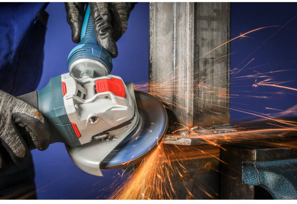 Person in Arbeitshandschuhen schleift eine Metallfläche mit einem Winkelschleifer, Funken fliegen, blauer Hintergrund.