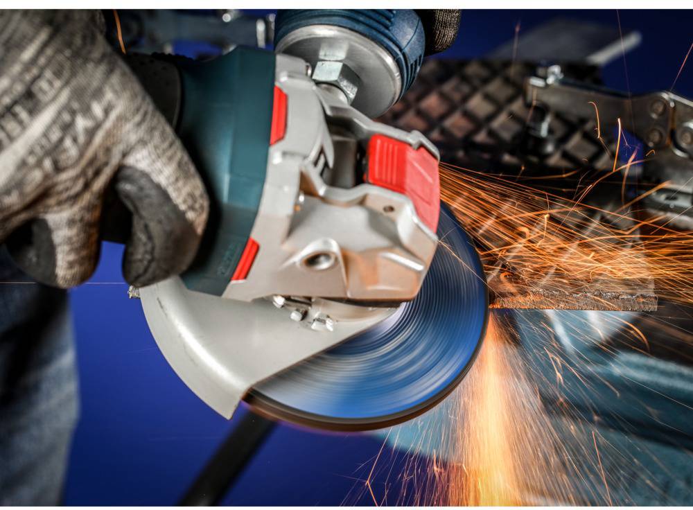 Person schleift Metall mit Winkelschleifer, Funken fliegen. Schutzhandschuhe tragen, Fokus auf Werkzeug und Funken, industrielle Umgebung.