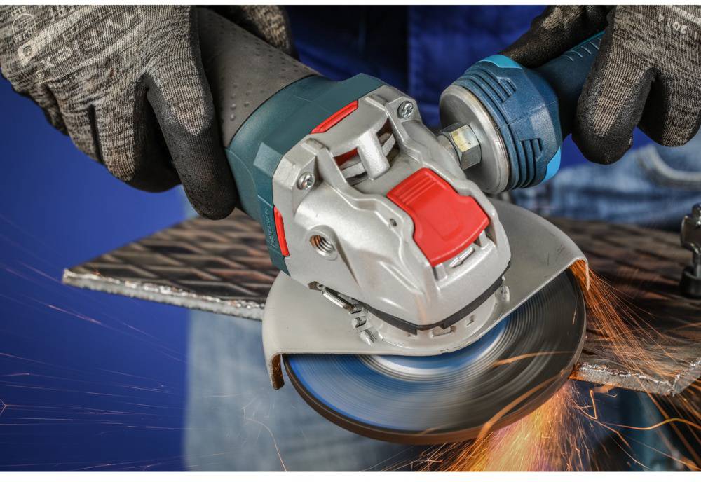 Person bearbeitet Metallplatte mit Winkelschleifer, Funken fliegen. Gerät hat blauen Griff und rotes Bedienelement, trägt Schutzhandschuhe.
