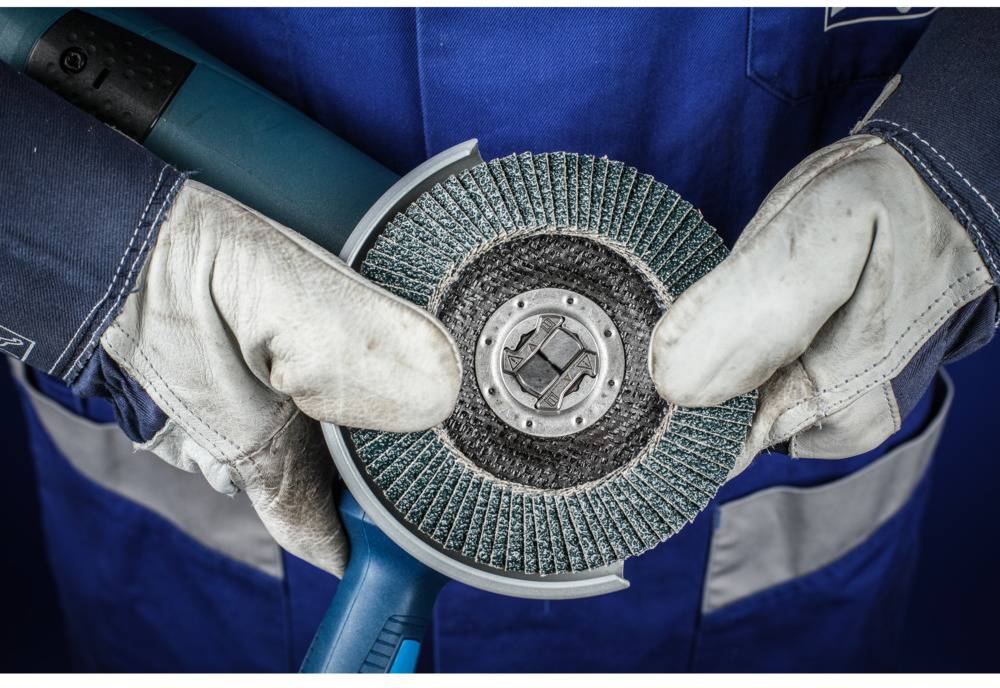 Arbeiter mit Schutzhandschuhen hält eine Schleifscheibe mit blauen Borsten. Gerät wird für Schleifarbeiten verwendet.
