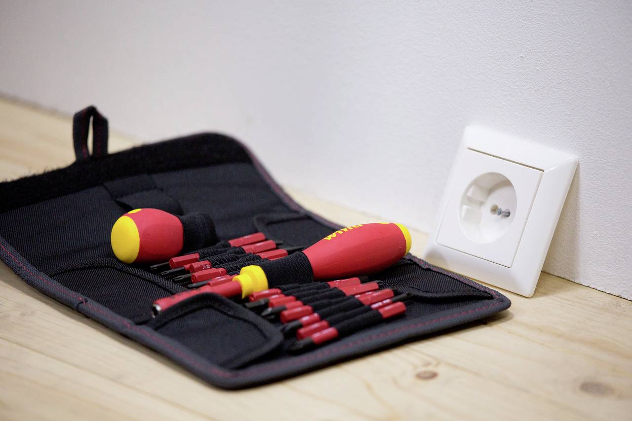 Ein aufgeschraubter Werkzeugkoffer liegt neben einer Steckdose. Das Set enthält mehrere rote Schraubendreher mit gelben Griffen.