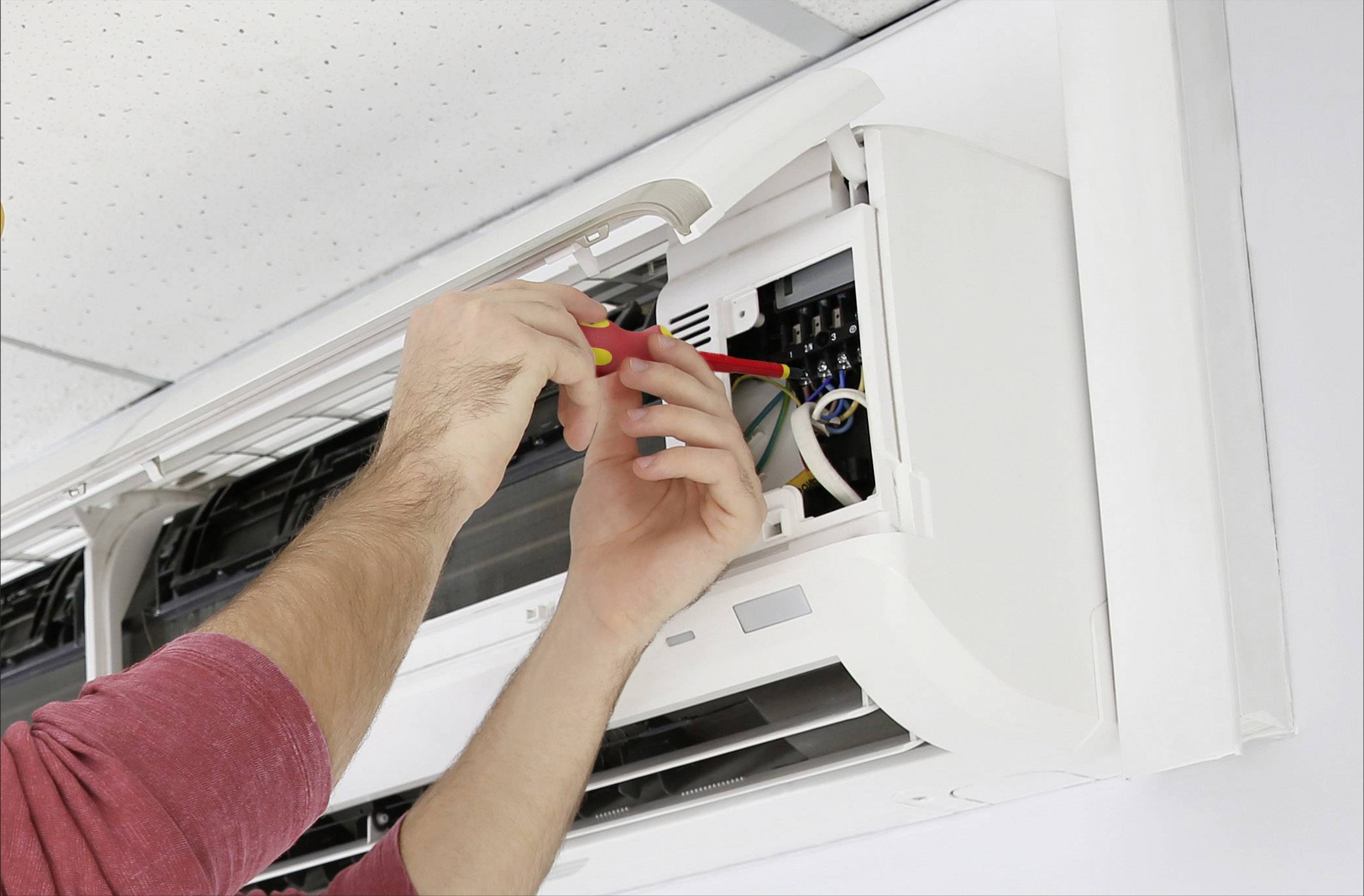 Eine Person repariert eine Klimaanlage an der Wand. Hände mit Schraubendreher arbeiten im Inneren des Geräts.