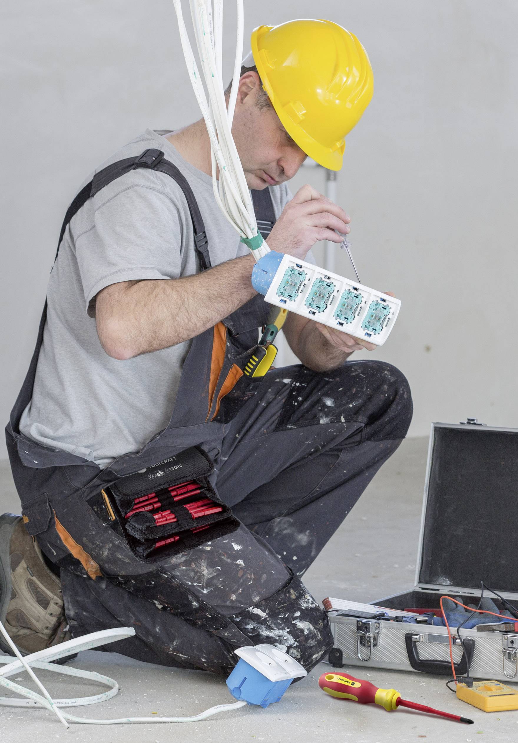 Ein Elektriker im gelben Helm arbeitet an einem Schaltschrank, umgeben von Werkzeugen. Er konzentriert sich auf die Verkabelung.
