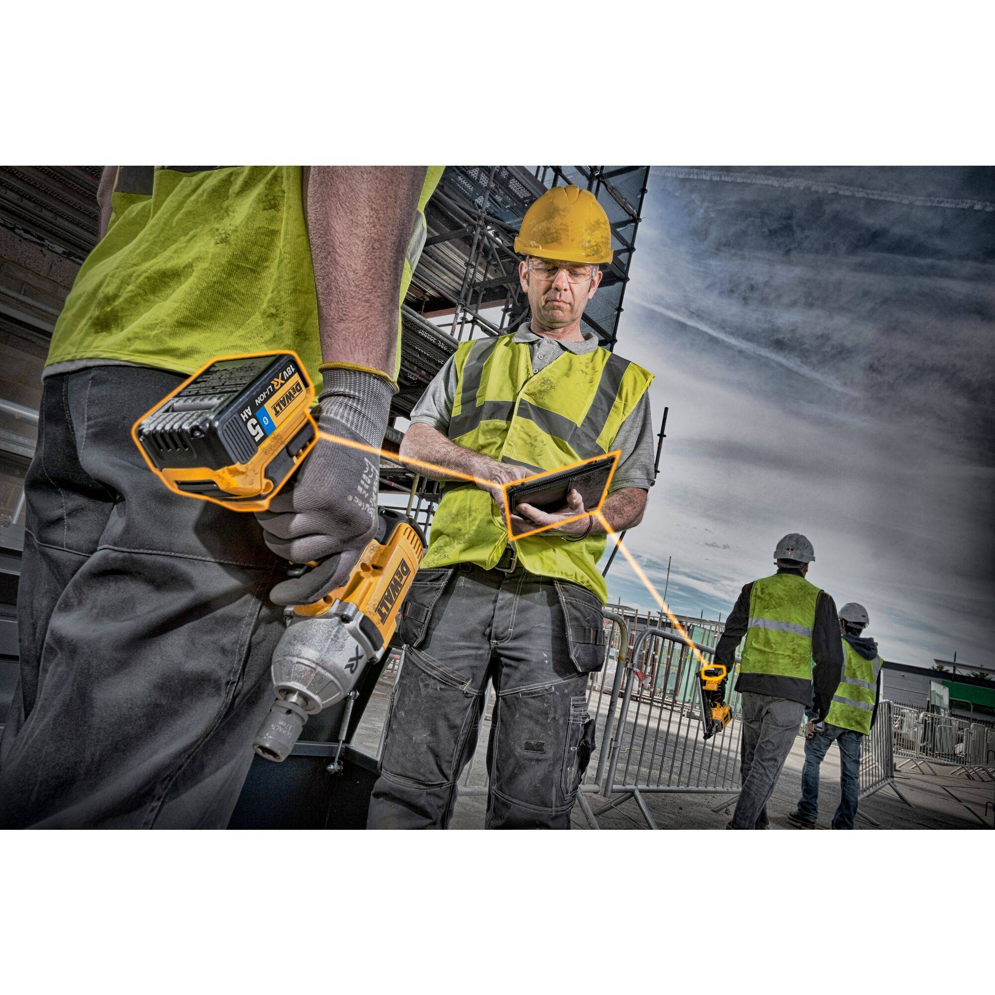 Drei Bauarbeiter mit Warnwesten und Helmen arbeiten auf einer Baustelle. Einer hält ein Tablet, während ein anderer ein Elektrowerkzeug hält.