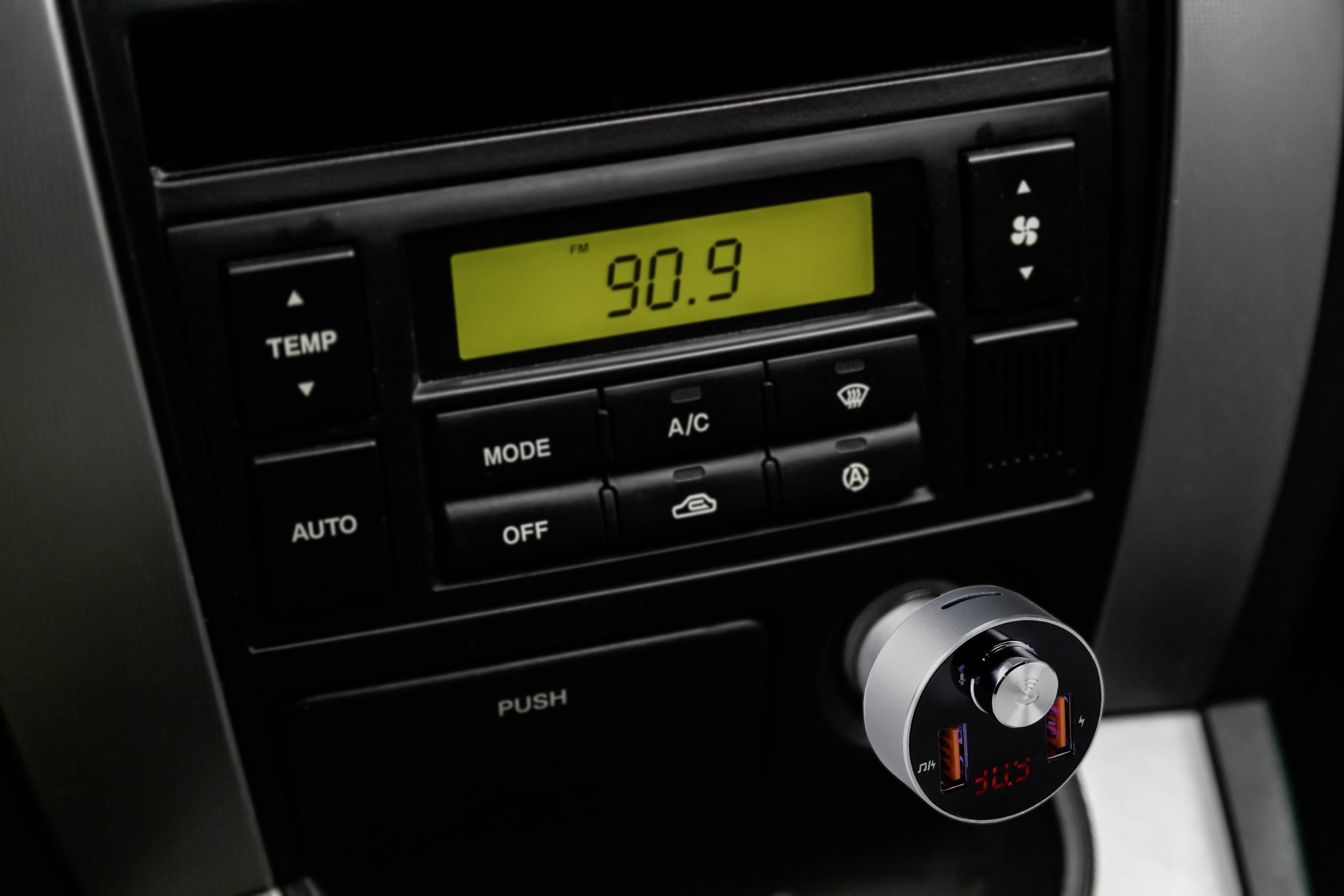 Auto-Radiodisplay zeigt Frequenz 90,9 an. Klimaanlagensteuerung darunter mit Temperaturregler, Moduswahl und Lüftungssymbolen.