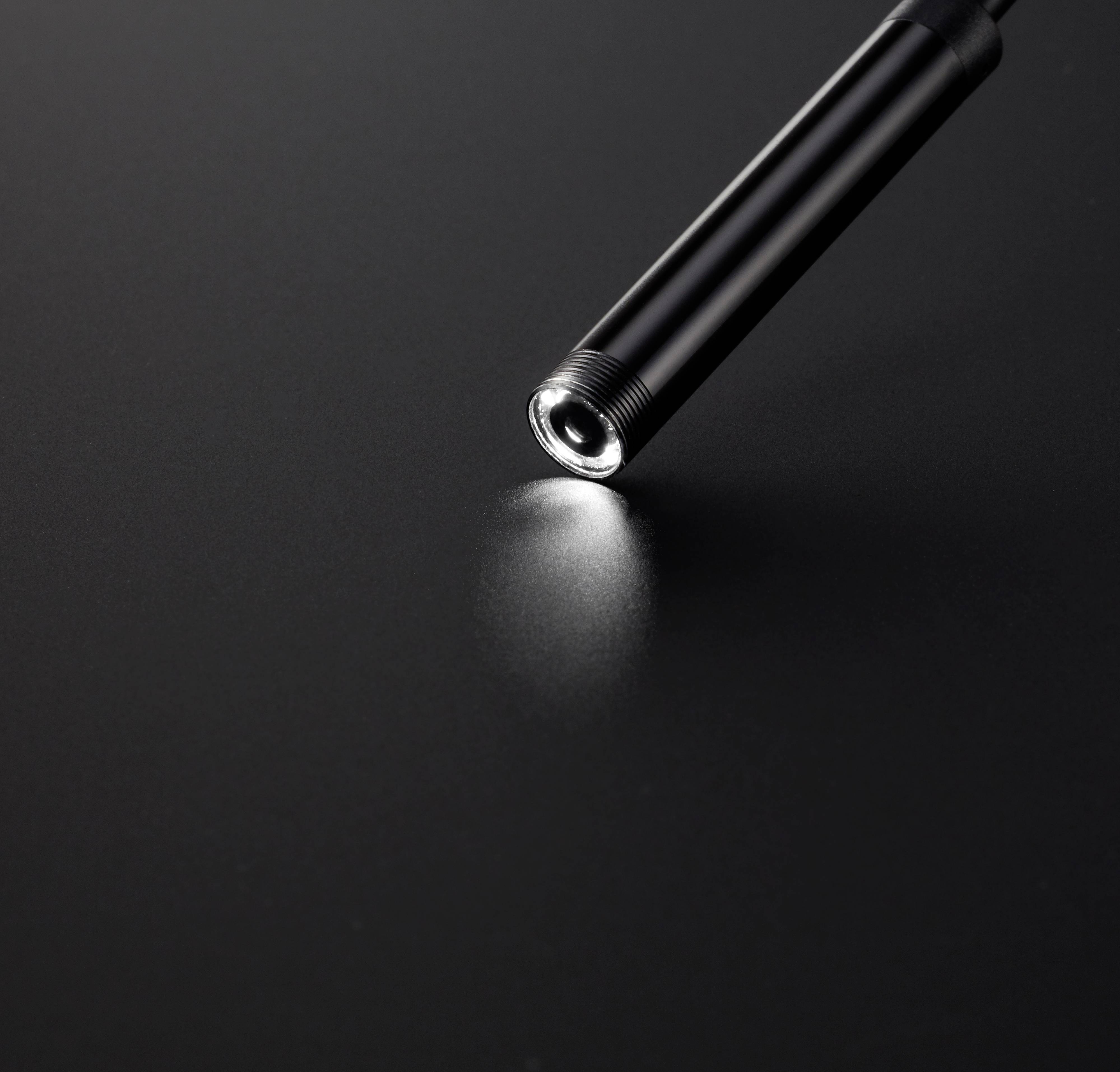 Eine kleine, schwarze Taschenlampe leuchtet auf einer dunklen Oberfläche und wirft einen Lichtkreis.