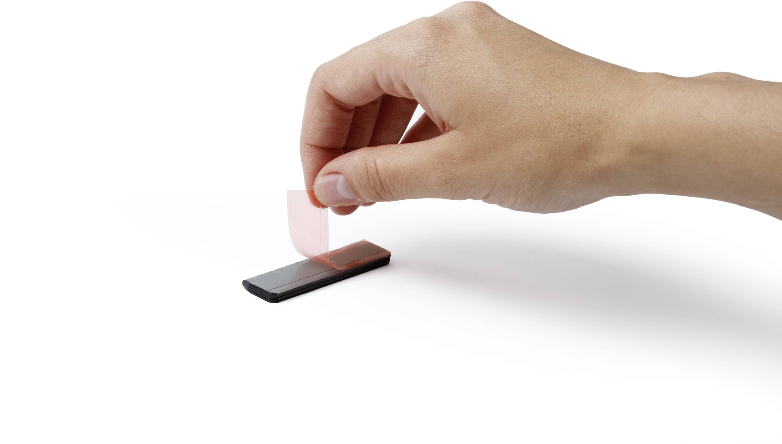 Eine Hand zieht ein Stück Klebeband von einem schwarzen Rechteck ab, möglicherweise demonstriert dies eine Technik oder Anwendung.