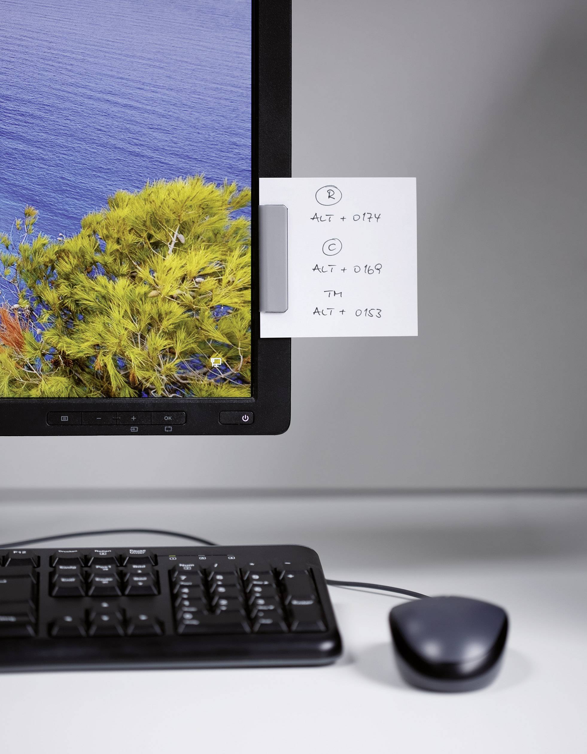 Auf einem Schreibtisch stehen ein Computerbildschirm mit einem Post-it-Notizzettel darauf, eine Tastatur und eine Maus. Der Zettel zeigt ALT-Tastenkombinationen.