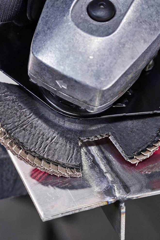 Ein Winkelschleifer bearbeitet ein Metallstück. Die Schleifscheibe entfernt Material vom Rand. Funken sind zu sehen.