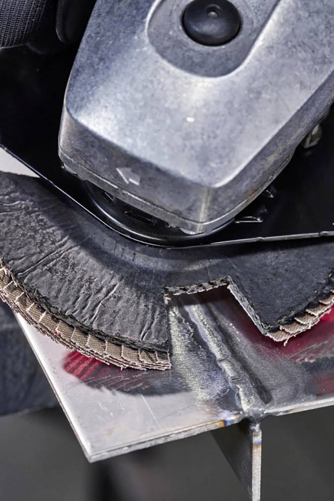 Nahaufnahme einer Schleifmaschine mit rundem Schleifkopf, die Kanten von Metallteilen abflacht. Focus auf die schneidende Bewegung.