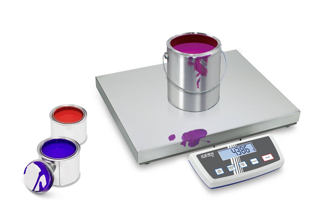 Eine Metallfarbdose mit roter Farbe steht auf einer digitalen Waage. Daneben zwei weitere Dosen mit roter und blauer Farbe. Die Anzeige zeigt '4386'.