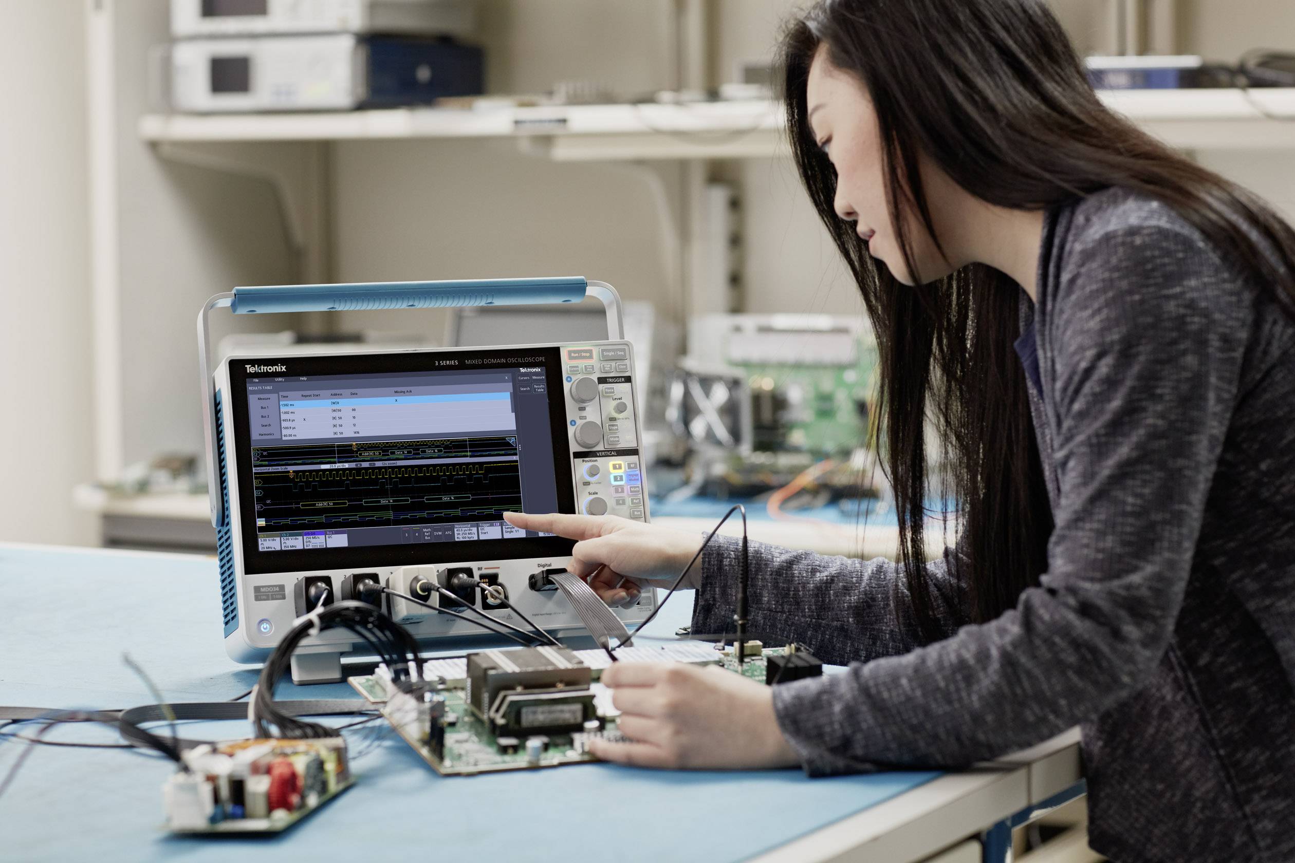 Eine Person arbeitet mit einem Oszilloskop an einer Leiterplatte in einem Labor. Sie überprüft elektronische Schaltkreise.