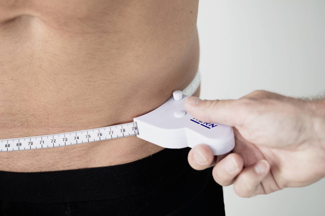 Ein Maßband wird um den Bauch eines Mannes gelegt, um den Taillenumfang zu messen.