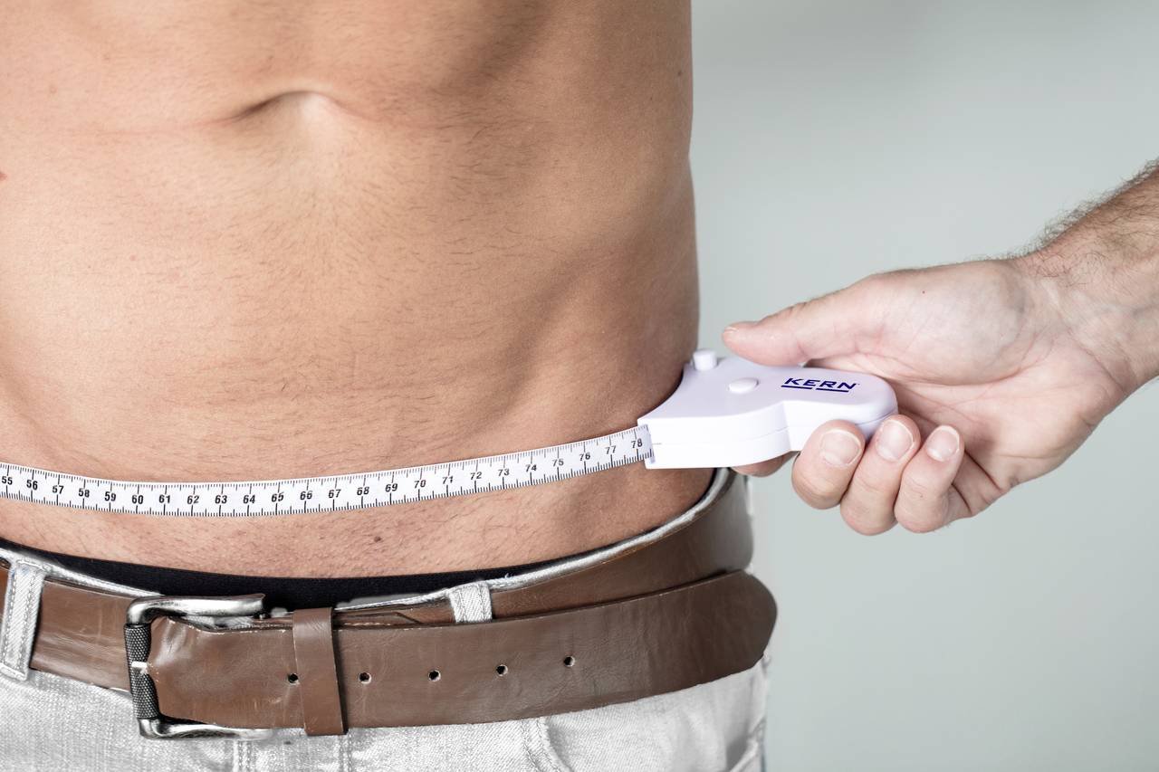 Mann misst seinen Taillenumfang mit Maßband, um den Gesundheitszustand zu überprüfen.