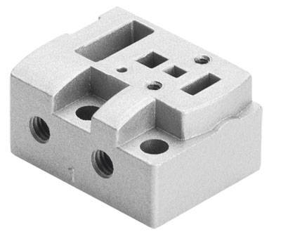 Metallblock mit mehreren eingelassenen Öffnungen und Aussparungen, wahrscheinlich als Montagesockel oder mechanisches Teil verwendet.