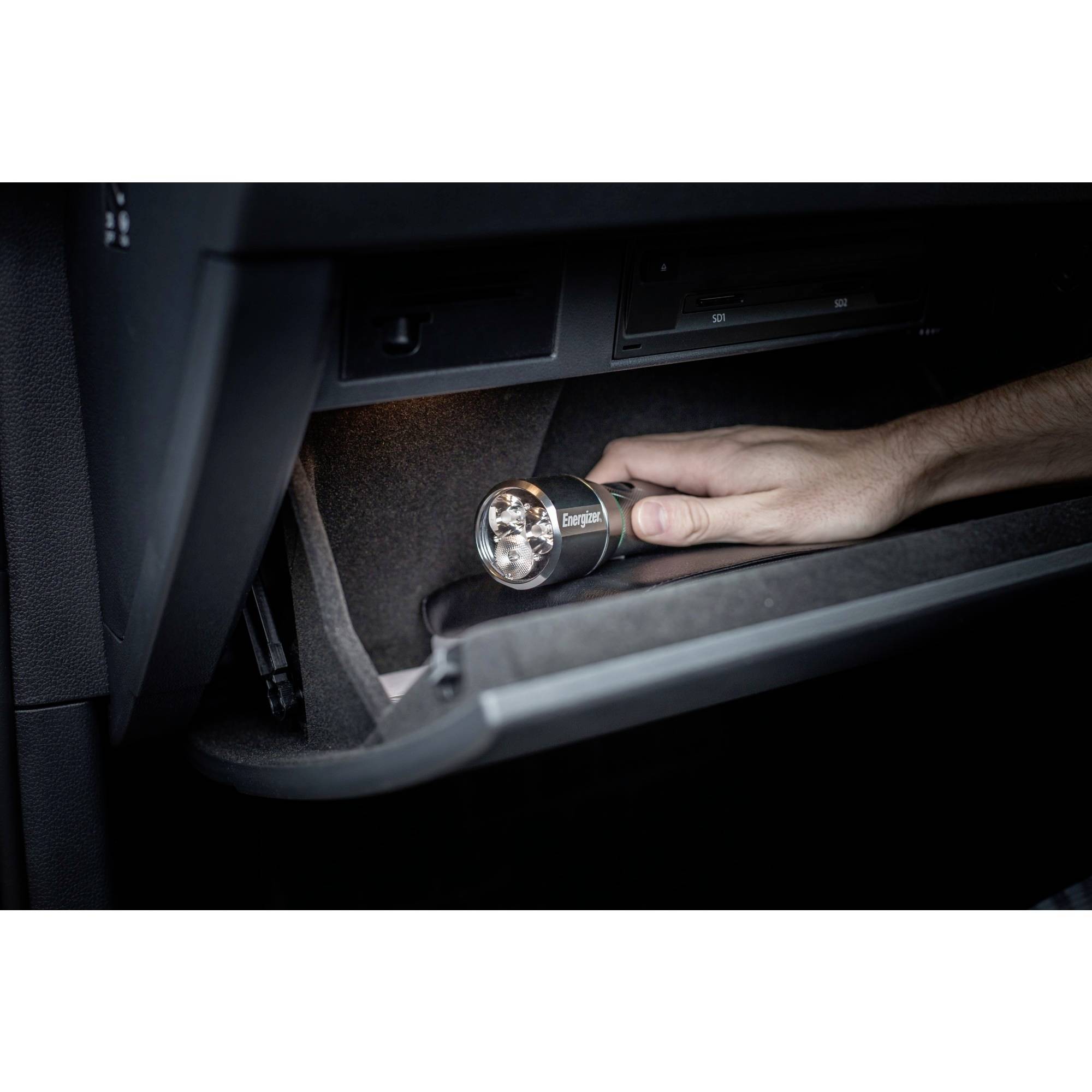 Eine Hand hält eine Taschenlampe im geöffneten Handschuhfach eines Autos und leuchtet den Innenraum aus.