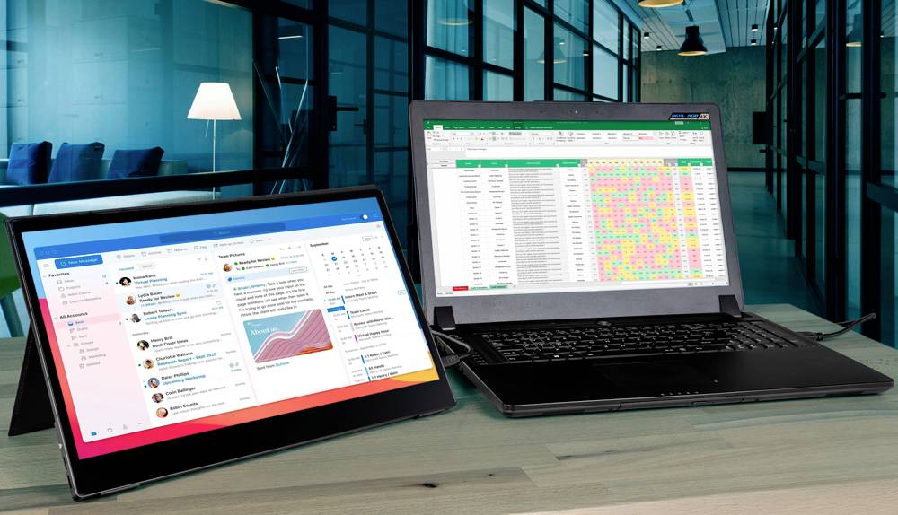 Ein Laptop und ein Tablet stehen auf einem Tisch. Der Laptop zeigt eine farbige Tabelle, das Tablet zeigt eine E-Mail-Ansicht. Im Hintergrund ein Büro.
