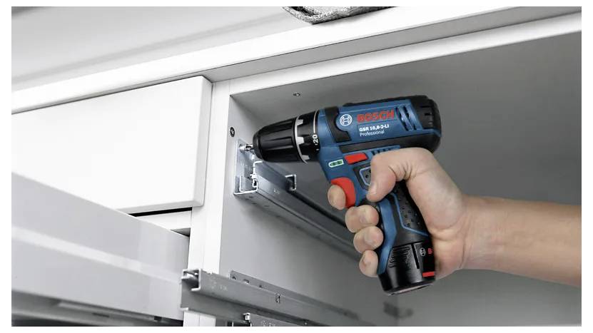 Eine Person benutzt einen Bosch Elektroschrauber, um Metallschienen in einem weißen Schrank zu installieren, was die Anwendung des Werkzeugs bei der Möbelmontage zeigt.