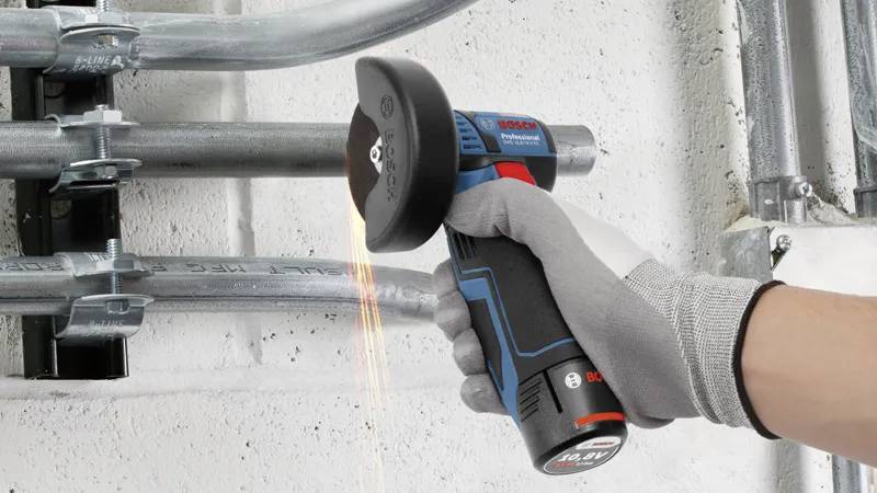 Eine Person, die einen Bosch-Winkelschleifer verwendet, um Metallrohre zu schneiden, wobei Funken sprühen. Die Person trägt einen grauen Handschuh zur Sicherheit.