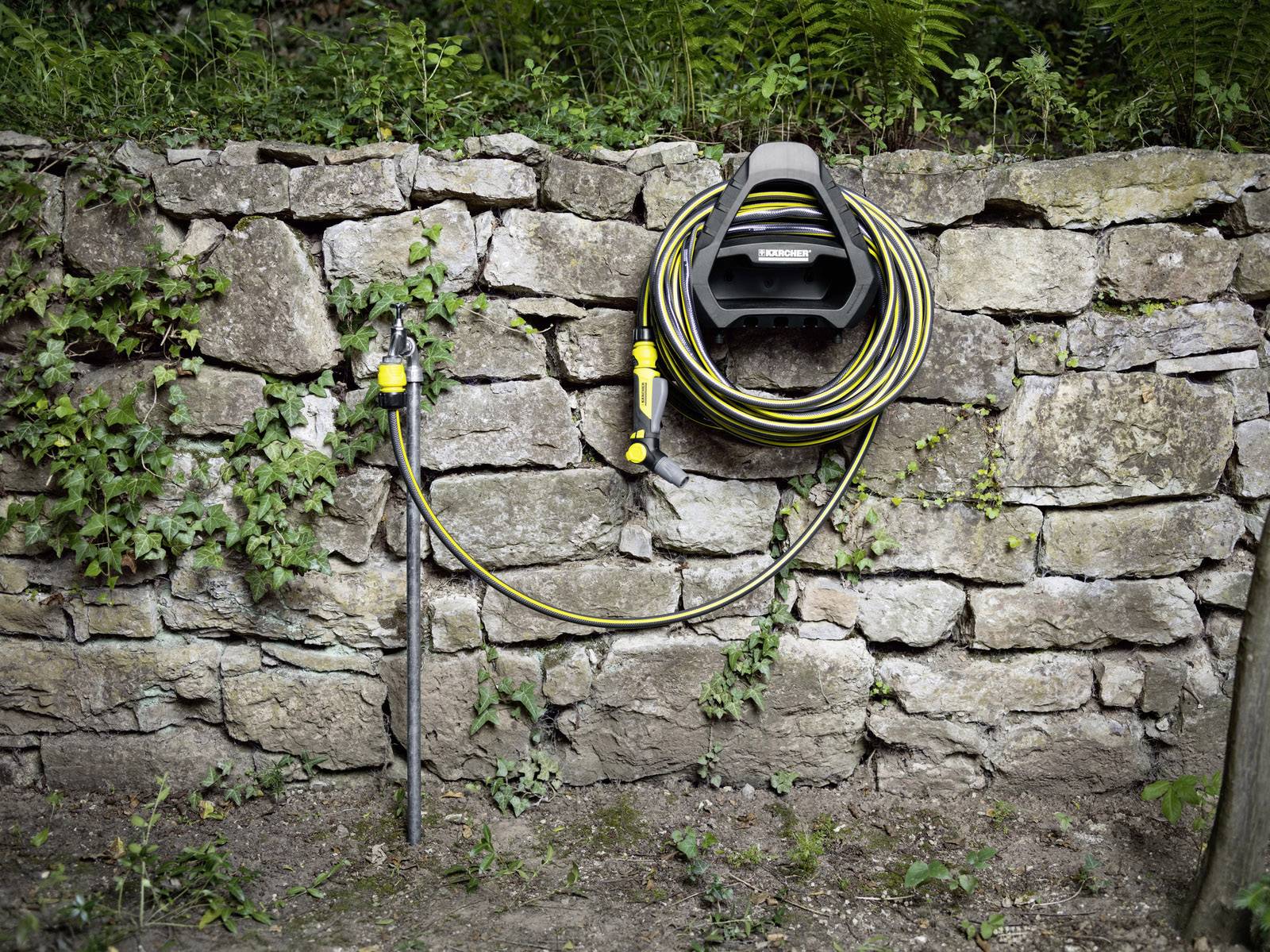 Gartenschlauchaufroller an einer Steinmauer montiert, mit einem aufgerollten gelb-schwarzen Schlauch und einem Wasserhahn.