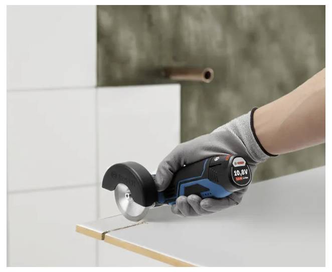 Mit Handschuh bekleidete Hand, die einen kabellosen Rotationsmesser verwendet, um eine weiße Fliese oder Platte auf einer Arbeitsfläche zu schneiden.
