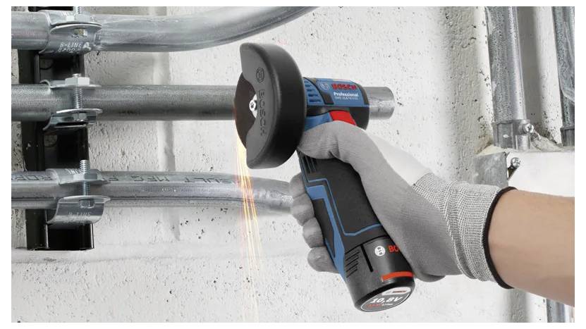 Behandschuhte Hand, die ein kabelloses Elektrowerkzeug mit einer Schneidscheibe an einem Metallrohr verwendet, wobei Funken in einem industriellen Arbeitsbereich entstehen.