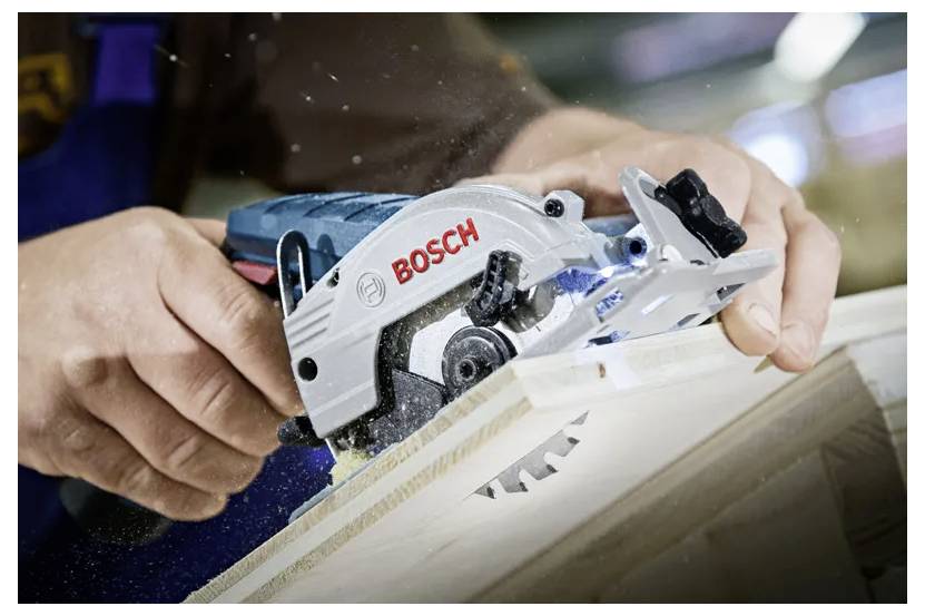 Eine Person verwendet eine Bosch-Kreissäge, um ein Holzbrett zu schneiden und demonstriert dabei präzise Holzbearbeitung in einer Werkstattumgebung.