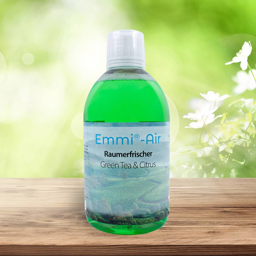 Eine grüne Flasche mit 'Emmi-Air Raumerfrischer Green Tea & Citrus' steht auf einem Holzuntergrund, im Hintergrund unscharfe Natur.