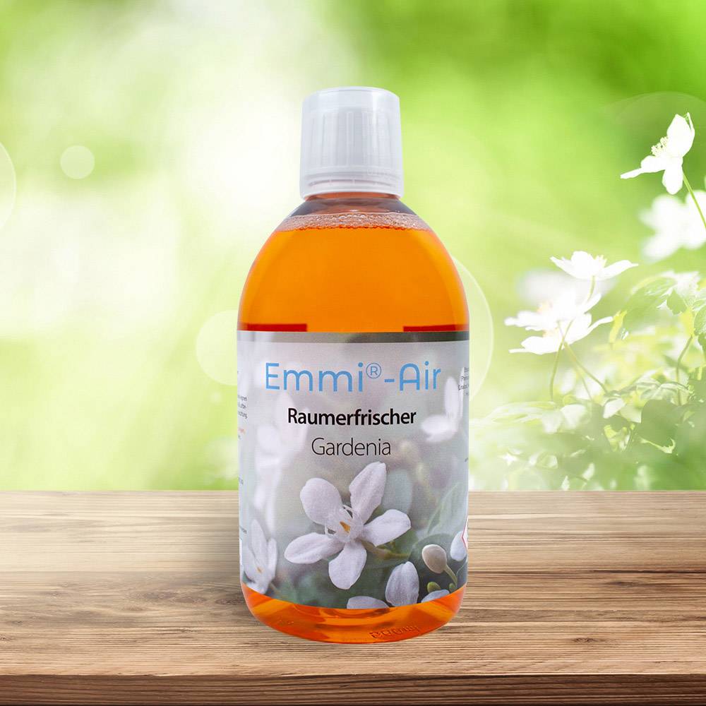 'Emmi-Air Raumerfrischer Gardenia' Flasche steht auf einem Holztisch vor einem verschwommenen grünen Hintergrund mit Blumen.