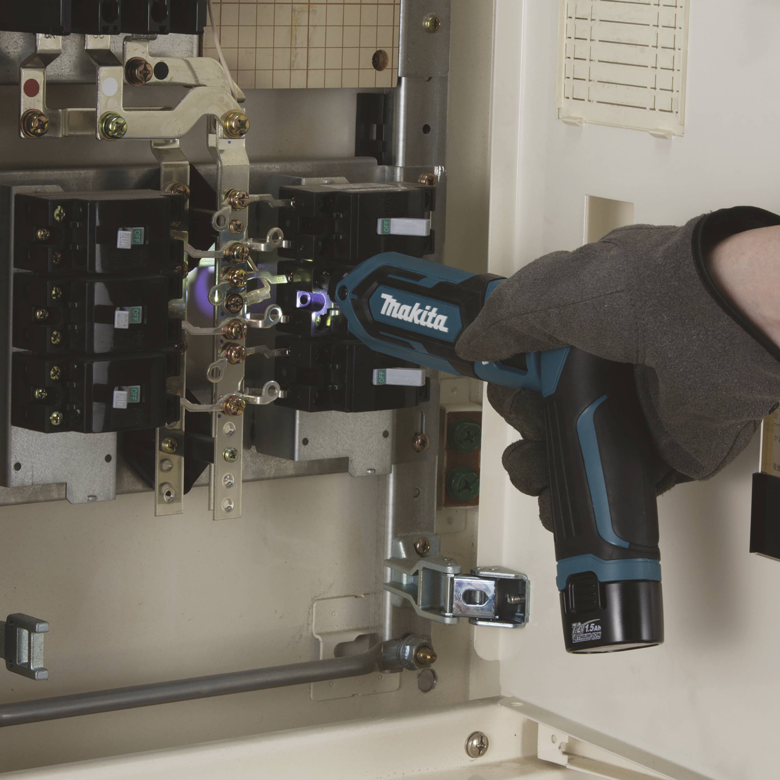 Eine Person mit Handschuh benutzt ein blau-schwarzes Elektrowerkzeug (Marke nicht themenrelevant) in einem Schaltschrank.