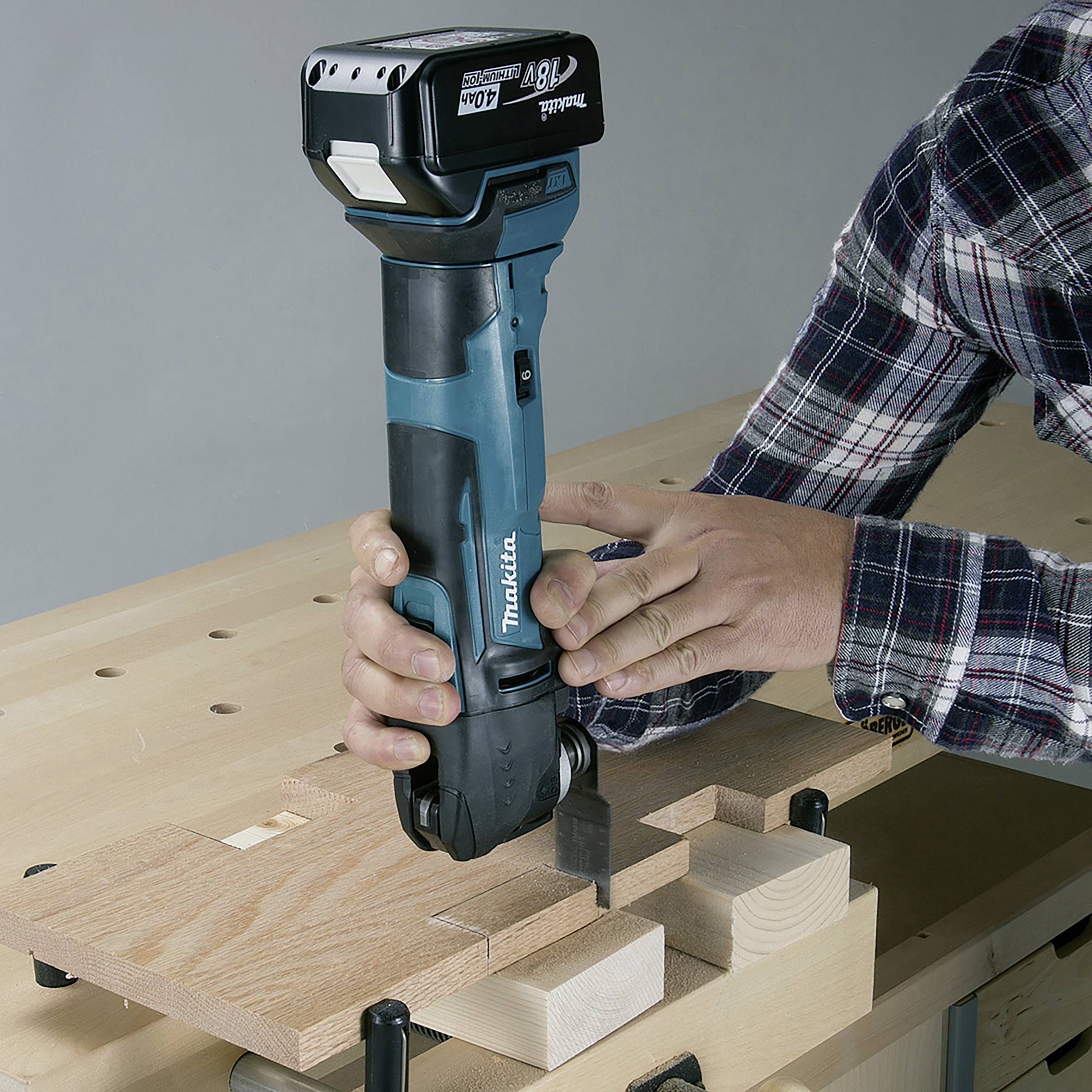Eine Person hält eine blaue Maschine in der Hand, die auf einem Holztisch eine Nut in ein Holzstück fräst.