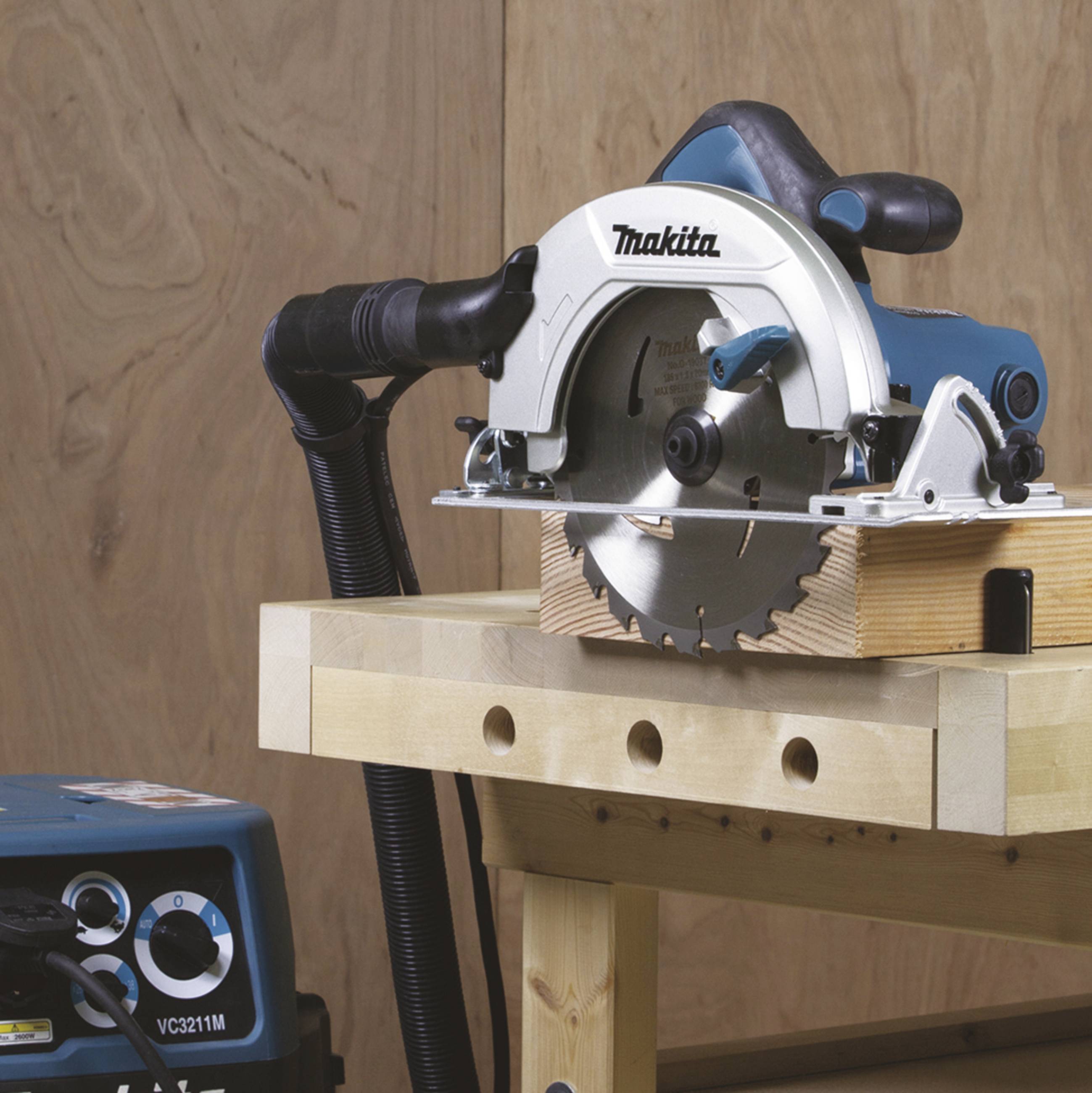 Elektrosäge auf einem Holztisch; bereit für Holzbearbeitung. Im Hintergrund ein Steuergerät mit Knöpfen und Anzeige.
