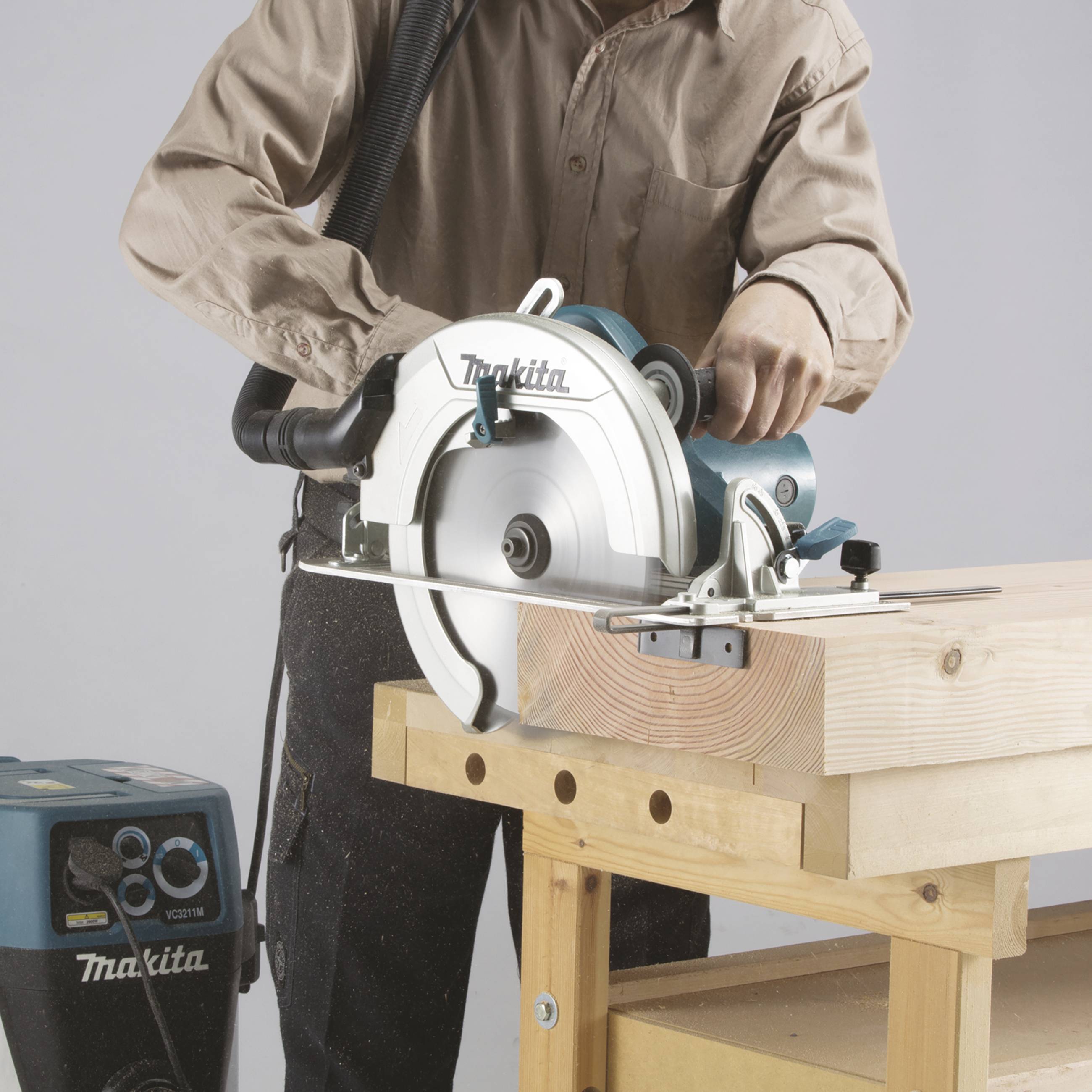 Eine Person bedient eine Kreissäge, um ein Stück Holz zu schneiden. Die Säge ist auf einem stabilen Holztisch befestigt.